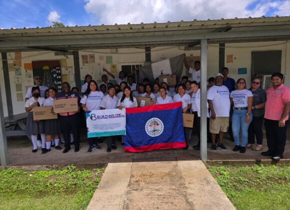 Build Belize volunteers and school staff with a Belize flag and boxes of donated supplies