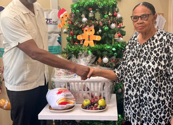 A Build Belize representative presenting a holiday gift basket beside a Christmas tree